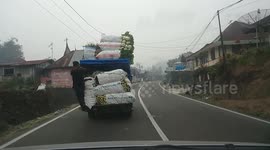 Man in Indonesia hangs off back of truck packed full of goods
