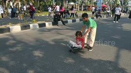 a boy collaborates with his younger sister to play skatebord on a car free day in the city of Padang