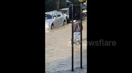 Man ties bin bags around legs as he wades through London floodwater