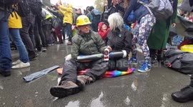 Extinction Rebellion London protesters with hands in a tube sit in the rain