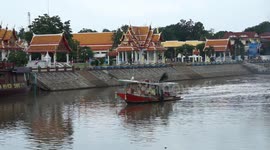 A small tug boat pulls a group of barges carrying sand, down a river and past a Buddhist Temple.