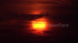 Birds fly past a big orange sunset in Thailand.