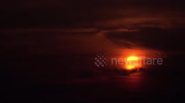 An airplane flies past a big orange sunset in Thailand.