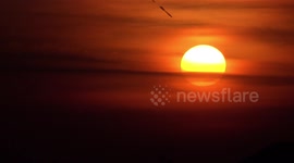 An airplane leaves a black trail in the sky at sunrise.
