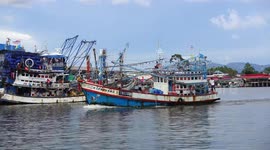 A Thai fishing boat sails into harbour, passing past hundreds of moored fishing boats.