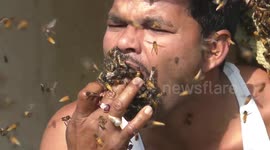 Indian honey collector stuffs shirt, mouth with live bees
