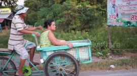 A man on a tricycle transports a lady.
