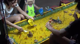 Adults and kids all having fun fishing at a night market in Thailand. They buy paper nets and need to be very skilful to catch a fish before the net disintegrates.