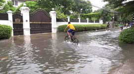 Kids on bicycles playing on a flooded Bangkok street and having great fun.
