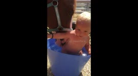 Baby taking a bath in horse bucket.