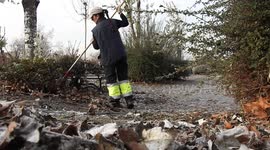 A woman gardener sweeps leaves in the park with a metal broom