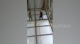 Thai airport security guard inches along glass ceiling to retrieve tourist's dropped phone