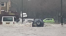 Vehicles drive through flood waters strewn with stranded cars