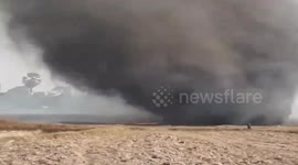 Thick cloud of smoke from grass fire blown across field by gust of wind in Thailand