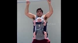 Six-month-old baby girl kicks legs while doing pull ups with super-fit dad