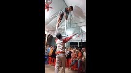Vietnamese street act dances while balancing metal bar with child on top on his mouth