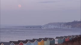 Full Pink Supermoon rising above Beach Huts in Kent, UK