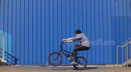 Cool young man wheelies with Mountainbike BMX Bike next to blue wall / Slowmo / Outdoor Action & Fun Sports