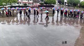 Chinese teachers hold umbrellas in a line for pupils during downpour
