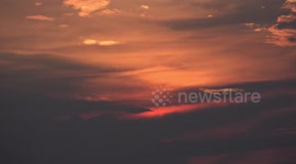 A small group of birds fly across an orange sky, just after sunset.