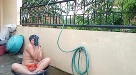 Young Asian boy cools down in a water basin and makeshift shower to beat the summer heat.