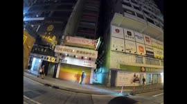 Protester shines torchlight on Mongkok police station as rubber bullets land near him and passerbys walk through