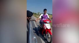 Thai policeman in car holds motorcyclist's hand to drag him home after his motorbike runs out of fuel