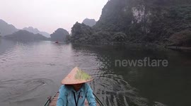 Woman squeezes boat through narrow gaps in the rock as tourists explore caves in Vietnam