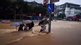 Chinese pedestrians hold hands and stand behind pole to avoid being washed away by flash floods
