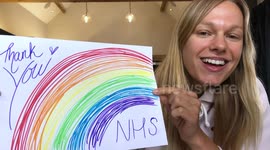 Cheerful female holding up rainbow drawing to thank healthcare workers during Covid-19 pandemic, looking at camera