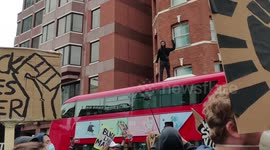 Boy climbs rooftop of bus at Black Lives Matter rally and is confronted by police, while protesters demand his release, chanting