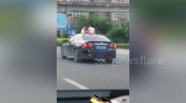 Twins spotted sitting on car roof as vehicle drives along busy road in China