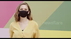 Portrait of pretty female wearing protective face mask looking at camera happy with multi coloured background
