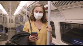 Young adult woman wearing protective medical face mask on underground train using mobile smart phone during coronavirus pandemic