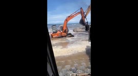 Smart excavator driver uses crane to rescue another vehicle being submerged by ocean waves