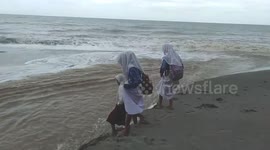 Schoolgirls wade through raging river gushing into the sea during Indonesia floods