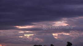An airplane flies across an evening sky with interesting cloud formations.