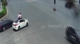 Chinese men sit on car roof as it drives along road