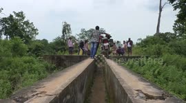 Indian villagers take bikes across narrow bridge 60 feet above nearby canal to leave home