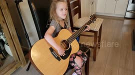 6 year old girl strumming an acoustic guitar