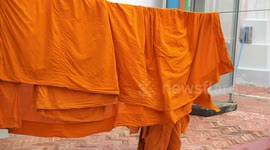 A young Buddhist monk collects orange robes from a clothes line.