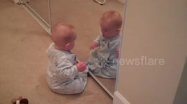 Baby bangs head on mirror in amazement with his own reflection