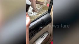 Family scoop cups full of water out of their car during floods in Cambodia