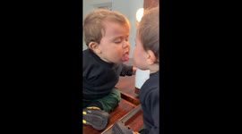 Adorable baby boy intrigued by reflection starts kissing himself in the mirror