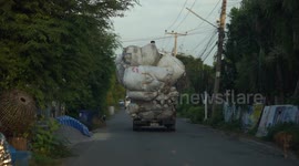 A man rides high on top of an overloaded recycle truck, and is thrashed by the tree tops.