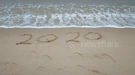 Goodbye 2020, the year 2020 scribbled on a sandy beach is washed away by the tide.