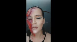 Woman using lipstick and chalk to makeup zombie face on halloween day