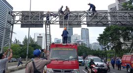 Police officers and firefighters evacuate a man who is climbing a 10-meter street signpost, Jalan Jenderal Sudirman, Central Jakarta, Indonesia