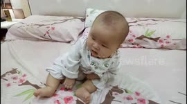 Adorable baby keeps fall down on bed while learns to sit for the first time