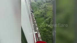 Motorcycle rider struck on railway bridge in Indonesia clings to the side to avoid oncoming train